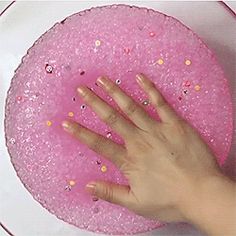 a person's hand on top of a pink cake with sprinkles