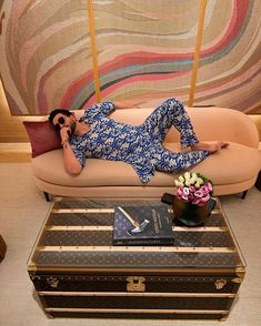 a woman laying on top of a couch next to an open suitcase and flower vase