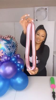 a woman holding up a pink balloon in front of a cake and balloons on a table