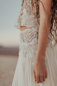 a woman in a white dress is holding her hand out to the side while standing on a beach