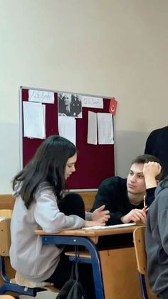 three people sitting at desks in a classroom with one person writing on a piece of paper