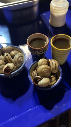 two bowls filled with clams next to a cup of coffee on a blue table