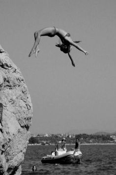 a person jumping off a cliff into the water from a boat in front of them