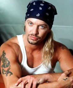 a man with long hair wearing a bandana and looking at the camera while sitting down