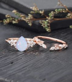 an opal and diamond ring sitting on top of a wooden table next to flowers