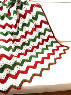 a crocheted afghan is sitting on a window sill next to a red, green and white blanket