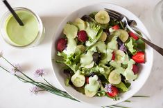 a white bowl filled with salad next to a glass of green juice and strawberries