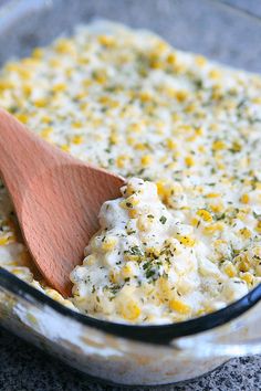 a wooden spoon in a casserole dish with corn and cheese on the side