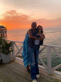 a man and woman hugging on a pier near the ocean