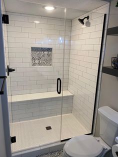 a white toilet sitting next to a walk in shower with glass doors and black handles