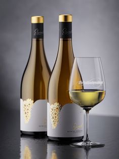 three bottles and two glasses of white wine on a table with a gray back ground