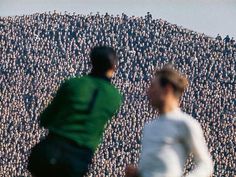 two men are playing soccer in front of a large group of people wearing green shirts