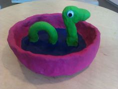 a green toy in a pink bowl on top of a table