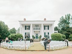 a group of people standing in front of a large white house with lots of chairs