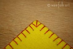 a close up of a yellow and red stitch on a wooden surface