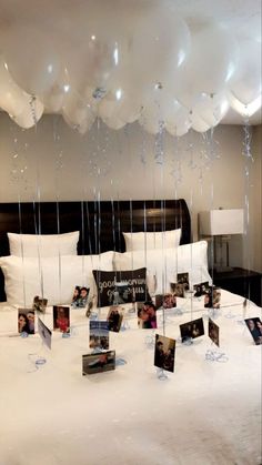 balloons are hanging from the ceiling above a bed with white sheets and pillows on it