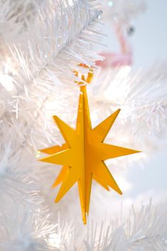 a yellow star ornament hanging from a white christmas tree