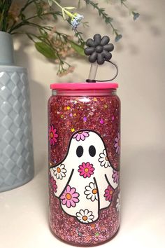 a glass jar with a flower decoration on it and a pink lid sitting next to a vase filled with flowers