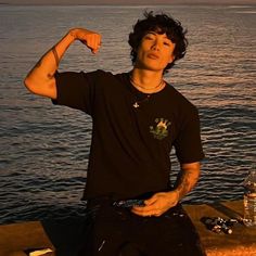 a young man sitting on the edge of a pier with his arm in the air