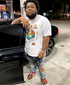 a man with dreadlocks standing in front of a car