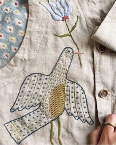 a person is stitching on a shirt that has flowers and birds embroidered on it