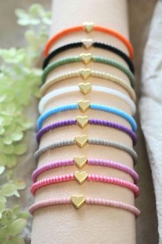 a stack of bracelets with gold hearts on each one and pink, blue, green, yellow, orange, red, white