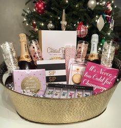 a christmas gift basket with champagne, chocolates and other holiday treats in front of a tree