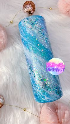 a blue and white liquid bottle with glitter on it sitting on a fluffy pink blanket