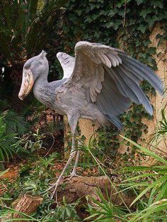 a statue of a bird with its wings spread out in front of some plants and trees