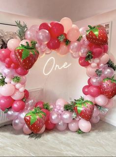 a strawberry balloon arch is decorated with pink and red balloons, green leaves, and strawberries