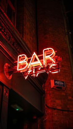 a neon sign that reads bar at night on the side of a red brick building