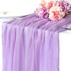 pink flowers are sitting on top of a purple table cloth next to a fork and knife