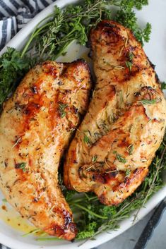 two pieces of chicken with herbs on the side in a white bowl next to a fork and knife