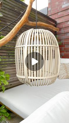 a birdcage hanging from a tree branch in front of a brick wall and white cushions