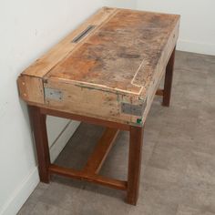 an old wooden table sitting on top of a tile floor next to a white wall