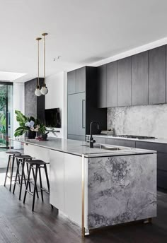 a kitchen with an island and bar stools in front of the counter top that has marble on it