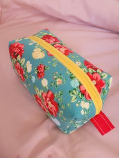 a blue flowered bag with yellow zipper is laying on a pink bedding sheet