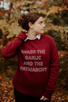 a woman wearing a red sweatshirt that says smash the garlic and the patriachy