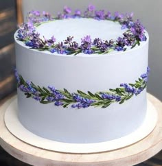 there is a white cake with purple flowers on the top and green leaves on the bottom