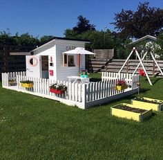 a small white house sitting on top of a lush green field next to a wooden fence