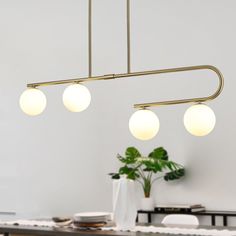 three lights hanging over a dining room table with white plates and plants in the background