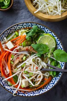 a bowl filled with noodles, carrots and green onions next to another bowl full of vegetables