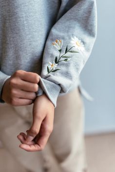 a person wearing a gray sweater with white flowers on it's sleeves and holding their hands together