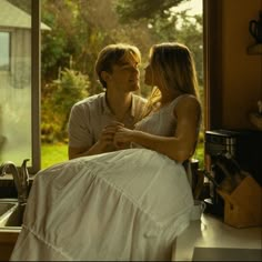 a man sitting next to a woman on top of a kitchen counter in front of a window