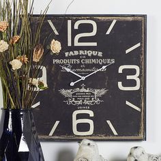 a black clock sitting on top of a table next to two vases with flowers