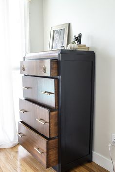 a dresser with drawers and pictures on top of it in front of a white wall