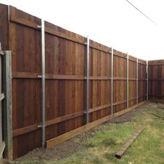 a wooden fence with metal posts on the sides and grass in the yard behind it