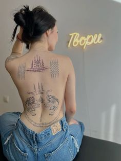 a woman with tattoos on her back sitting in front of a sign that reads topple