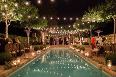 an outdoor wedding with candles and lights around the pool