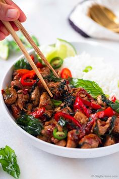 someone is holding chopsticks over a bowl of food with meat and veggies